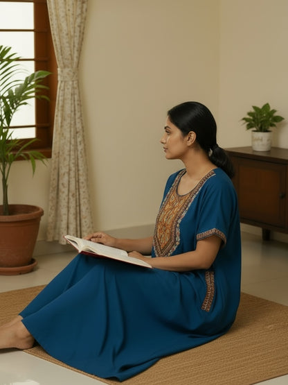 Kishona deep blue ethnic kaftan with multi-coloured embroidery, worn by a woman reading on a rug in a home setting.